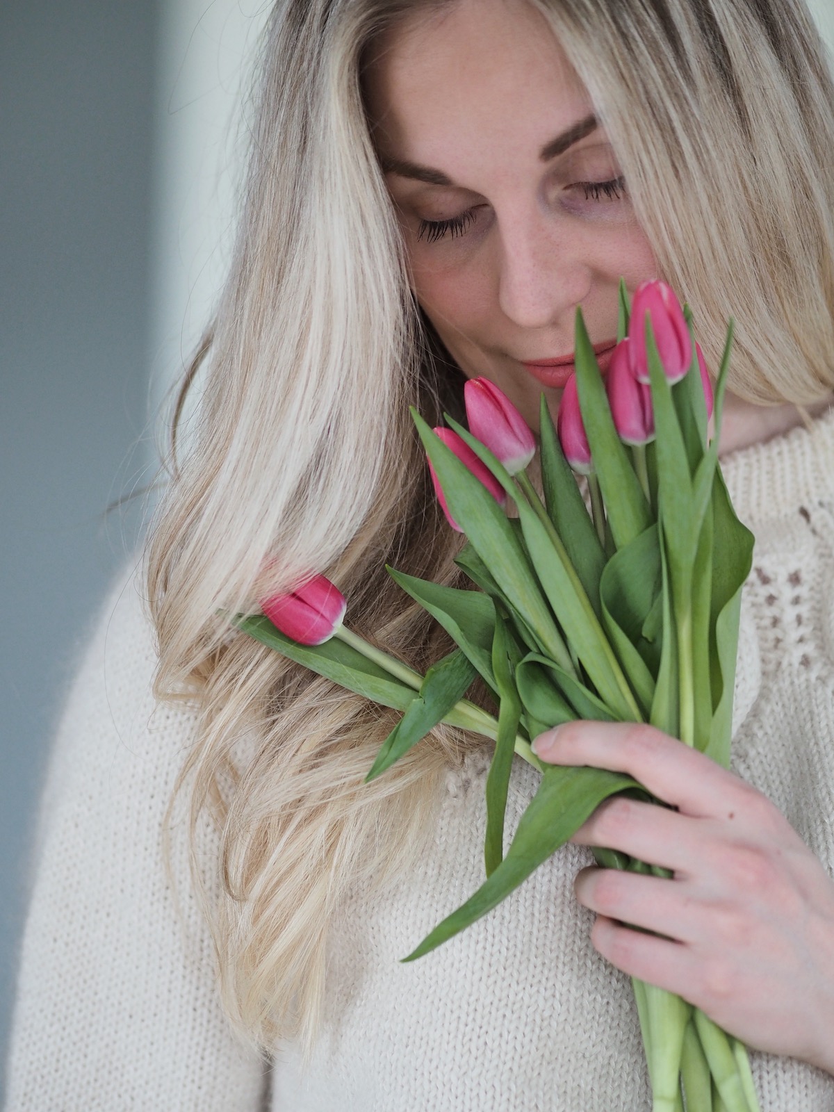 jente med krøllet hår iført dahliagenser som lukter på en bukett rosa tulipaner