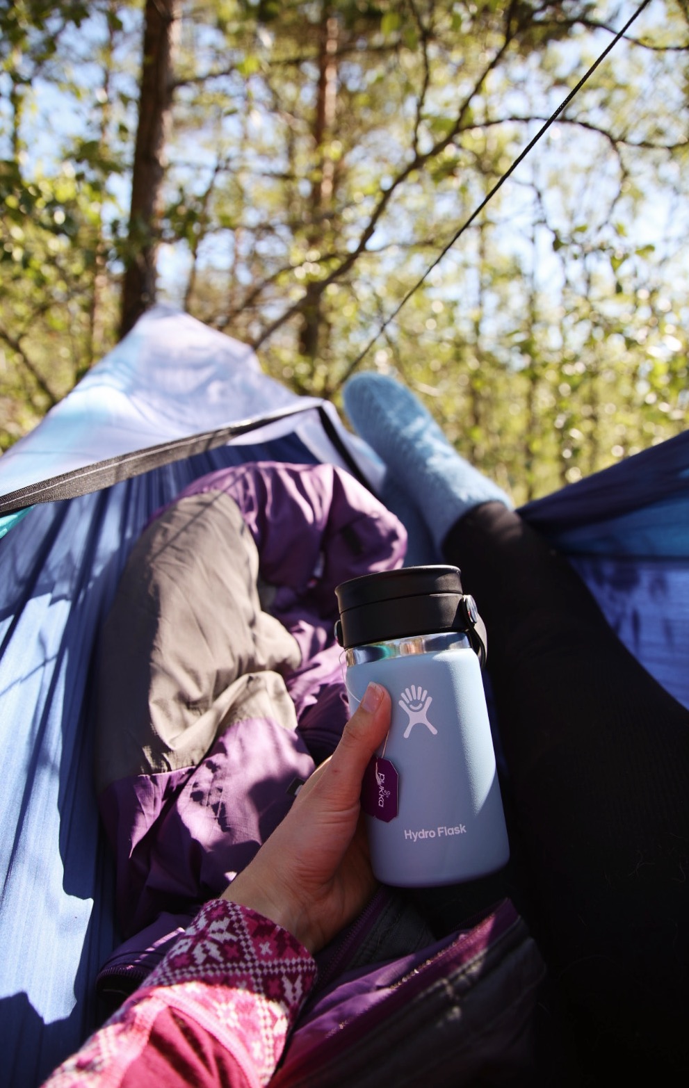 laying in hammock with a hydro flask coffee cup, a sleeping bag and growing rib socks.